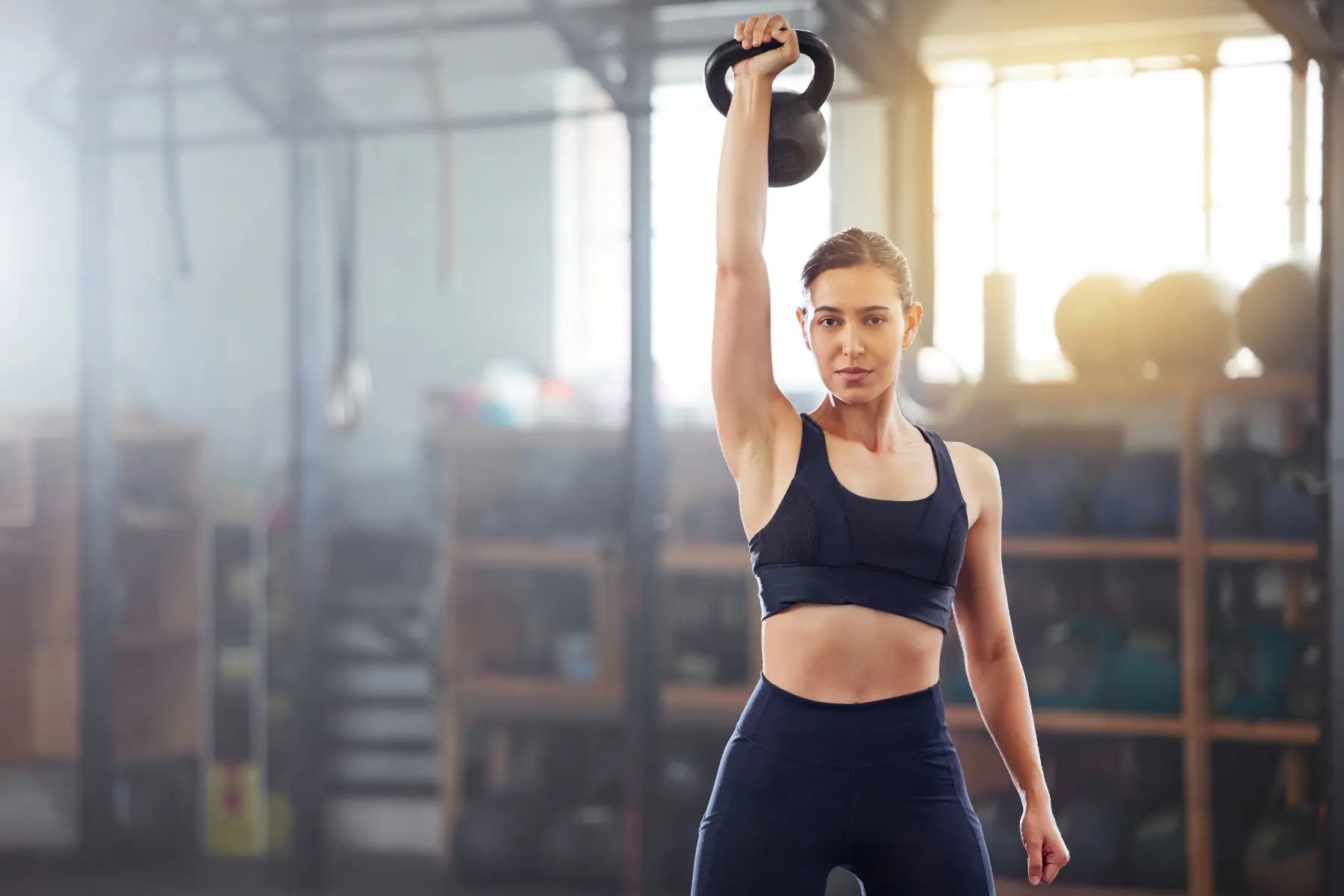 Bone health for women shown through strength training with a woman lifting a kettlebell in a gym.