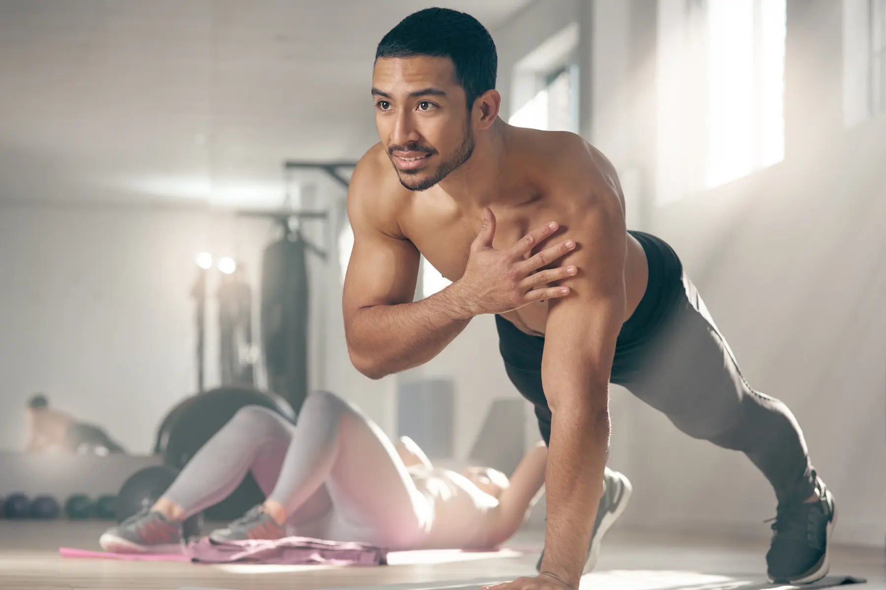 Body composition tracking progress shown by a lean, shirtless man holding a single-arm plank position on a gym floor.