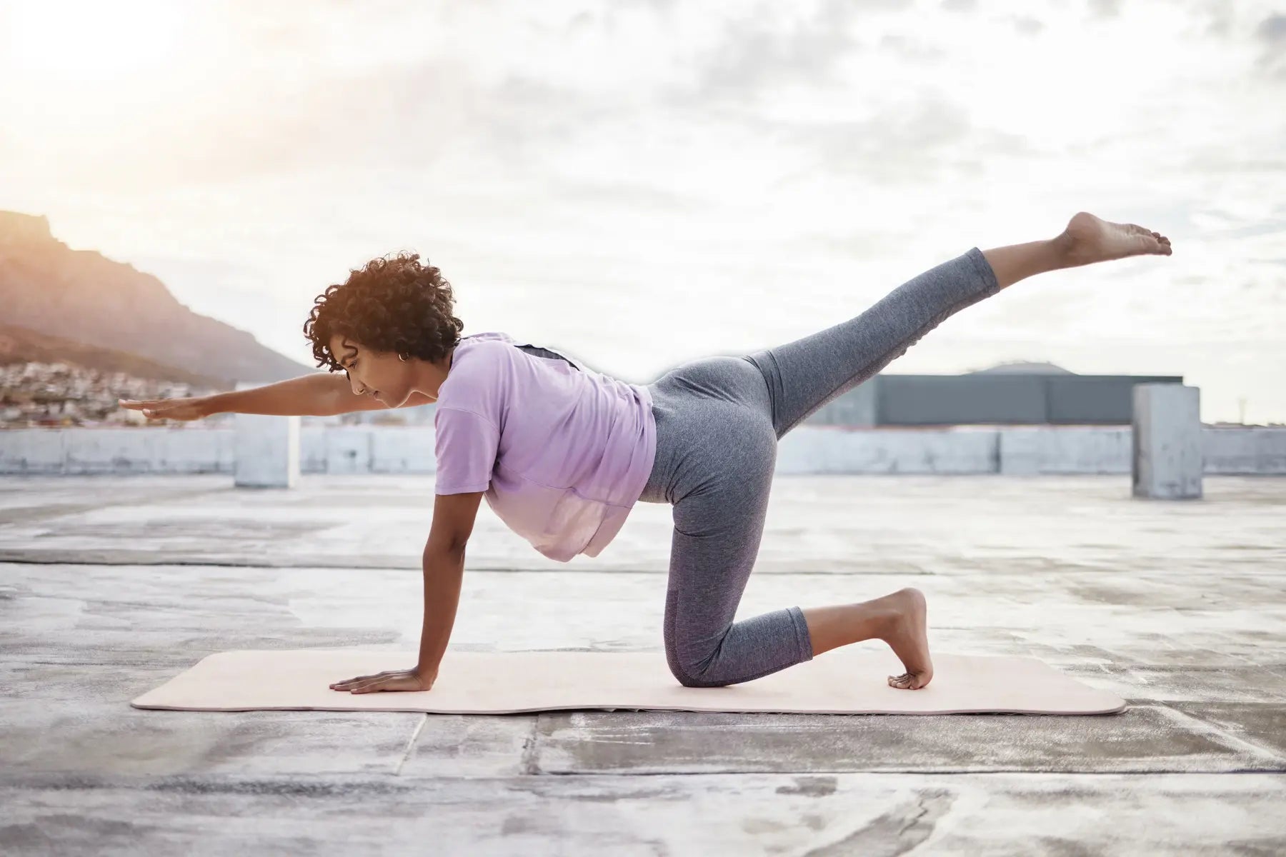 Body composition workout being performed by a woman in a bird-dog pose on an outdoor rooftop with mountain views.