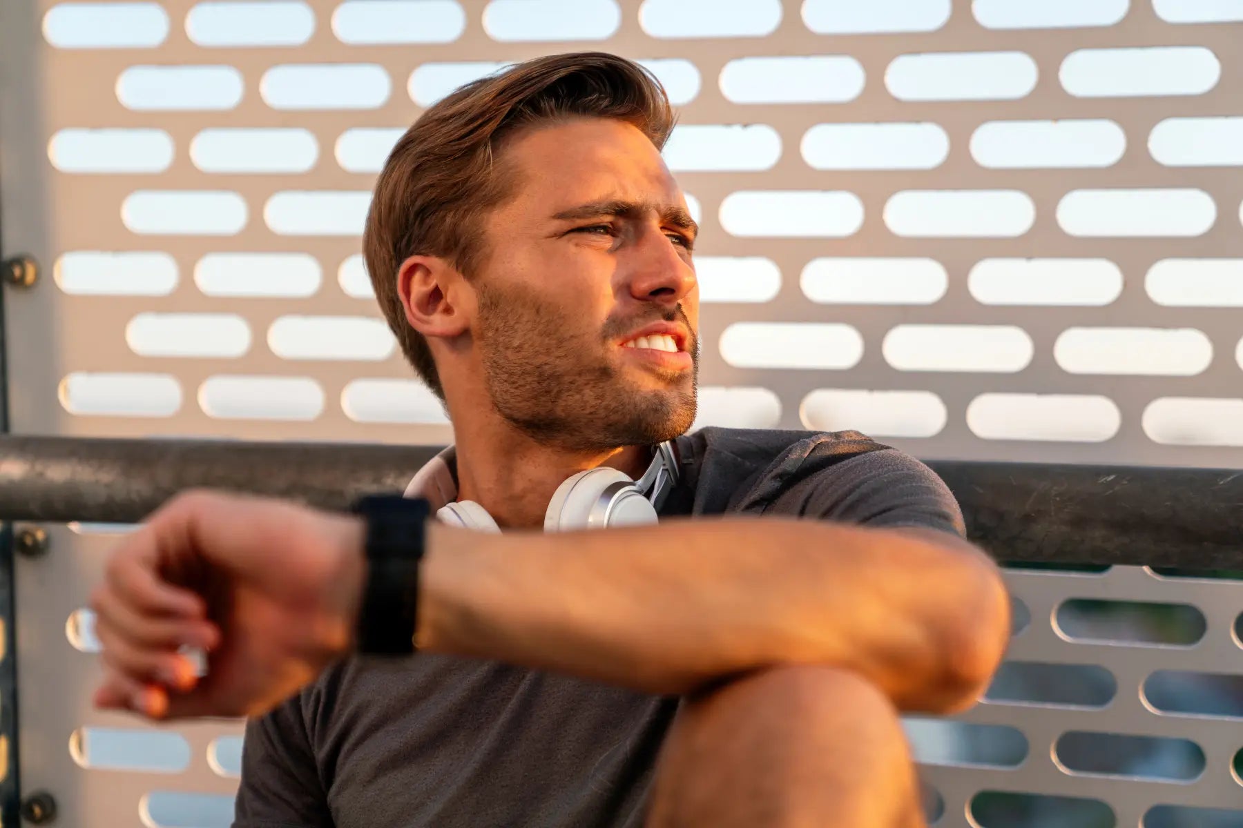 Body composition scanning preparation with a fit man resting outdoors wearing headphones and checking his smartwatch.