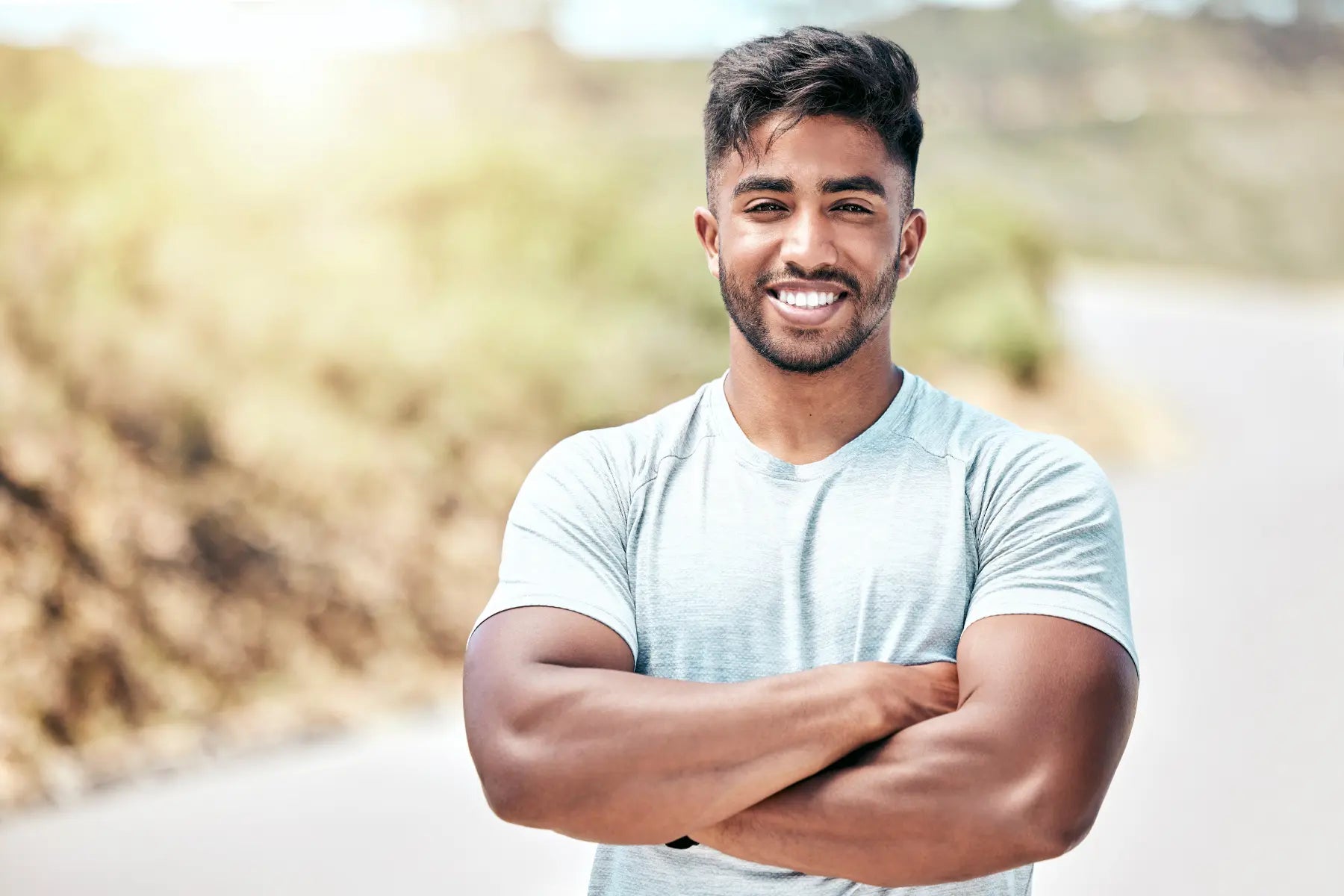 Body fat measurement results reflected by a fit smiling man with crossed arms standing on a sunlit outdoor road in athletic wear.