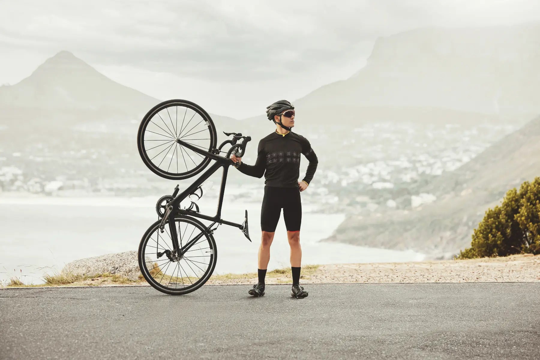 DEXA body composition training as cyclist poses confidently holding bike upright on scenic mountain road.