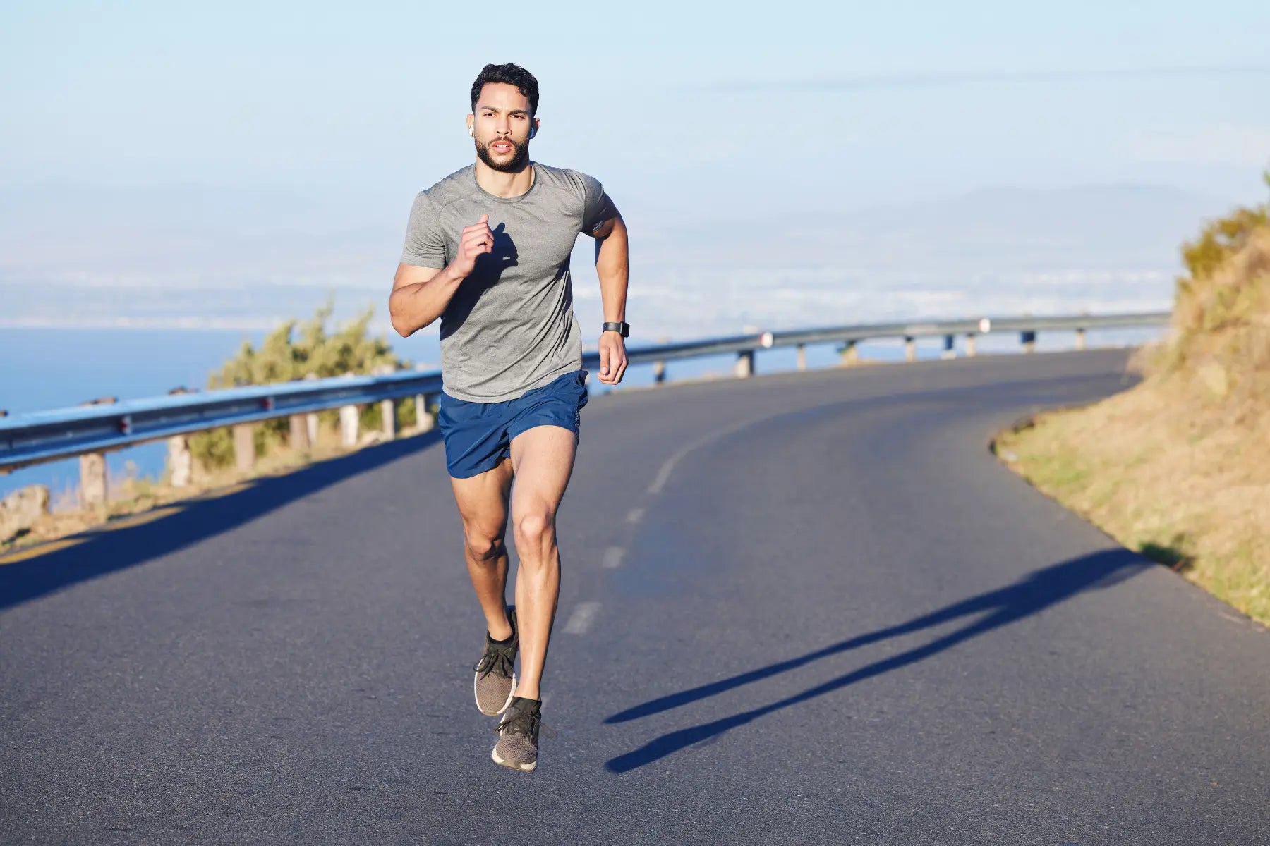 DEXA scan fitness preparation as athletic man runs uphill on a coastal road wearing smartwatch and workout gear.