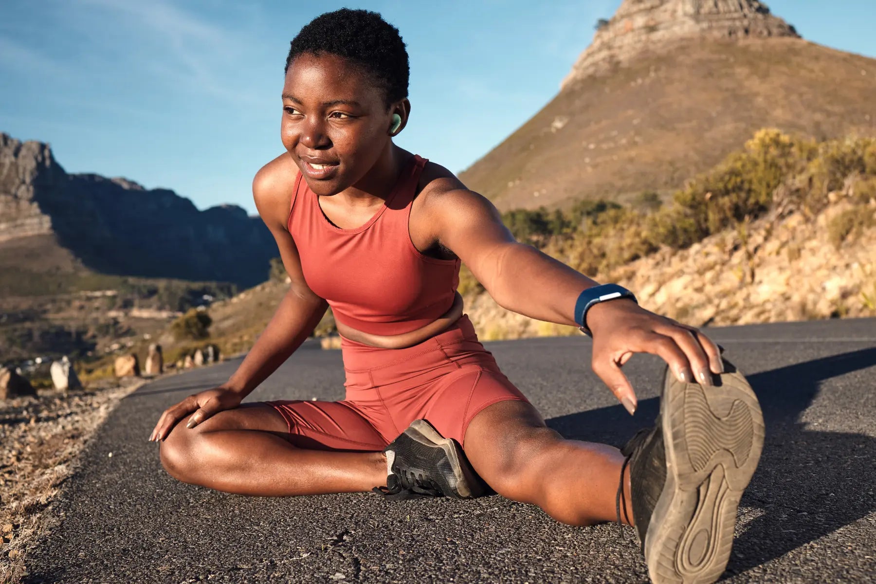 DEXA scan for body fat preparation as woman stretches on mountain road wearing fitness tracker and athletic outfit.