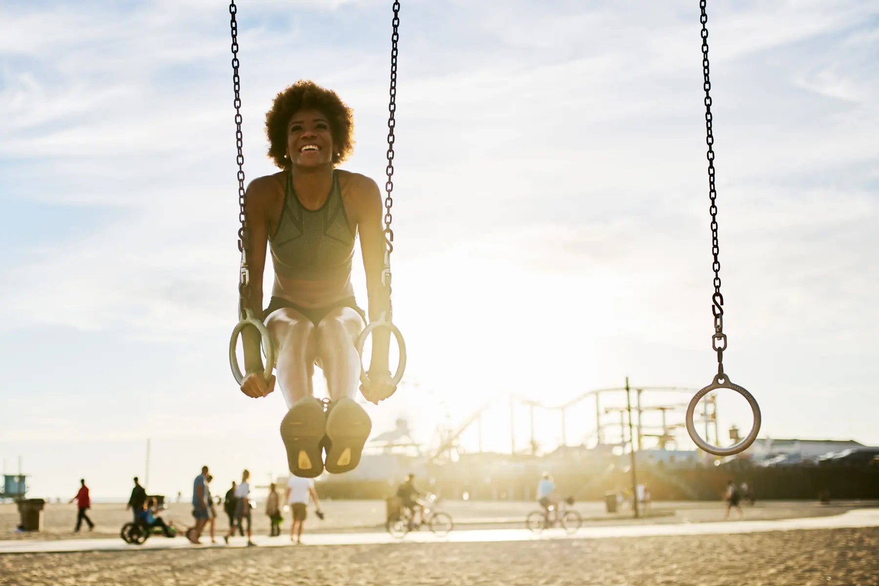 DEXA scan for bone density training as woman performs strength exercise on gymnastic rings at the beach during sunset.