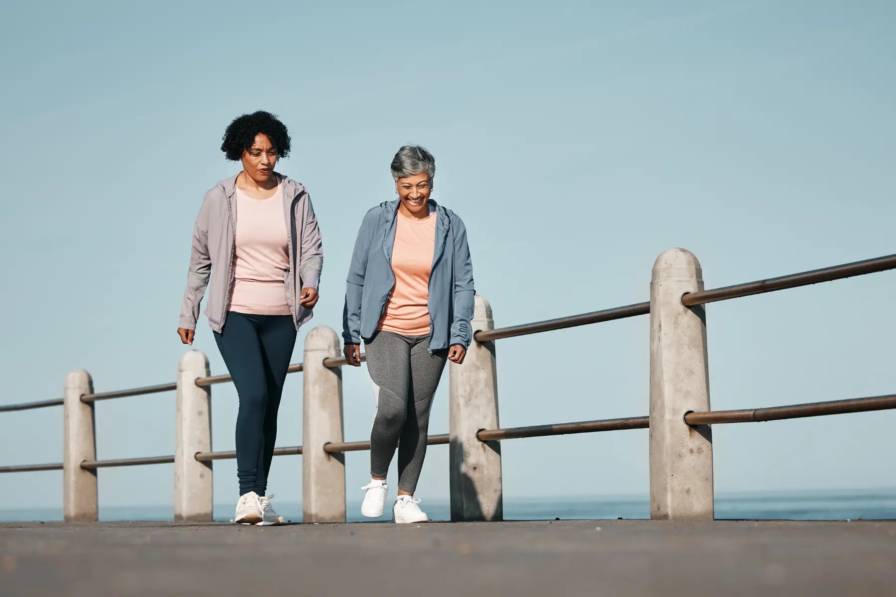 DEXA scan for bone health supports active aging as two older women walk briskly along a seaside promenade.