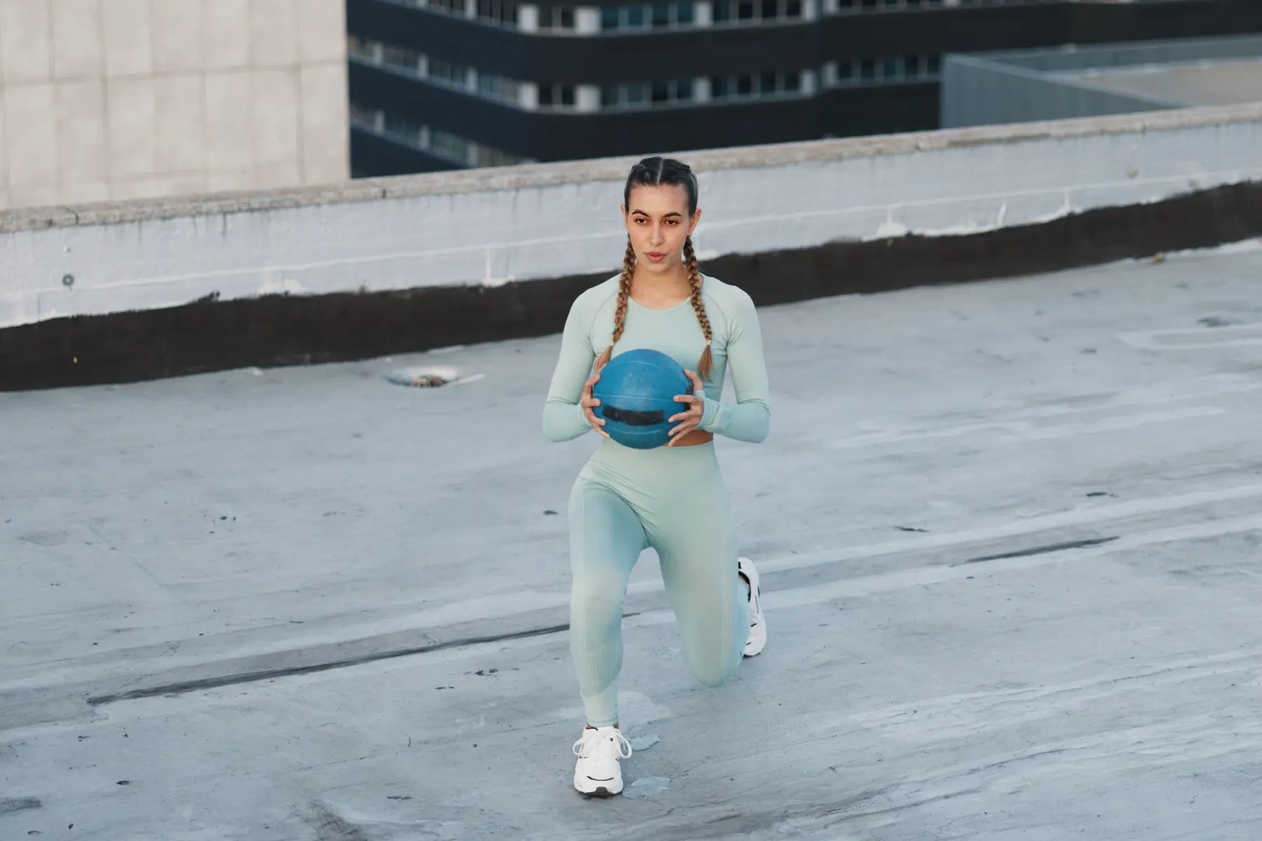 DEXA scan results preparation as woman in activewear performs lunge exercise with medicine ball on rooftop.