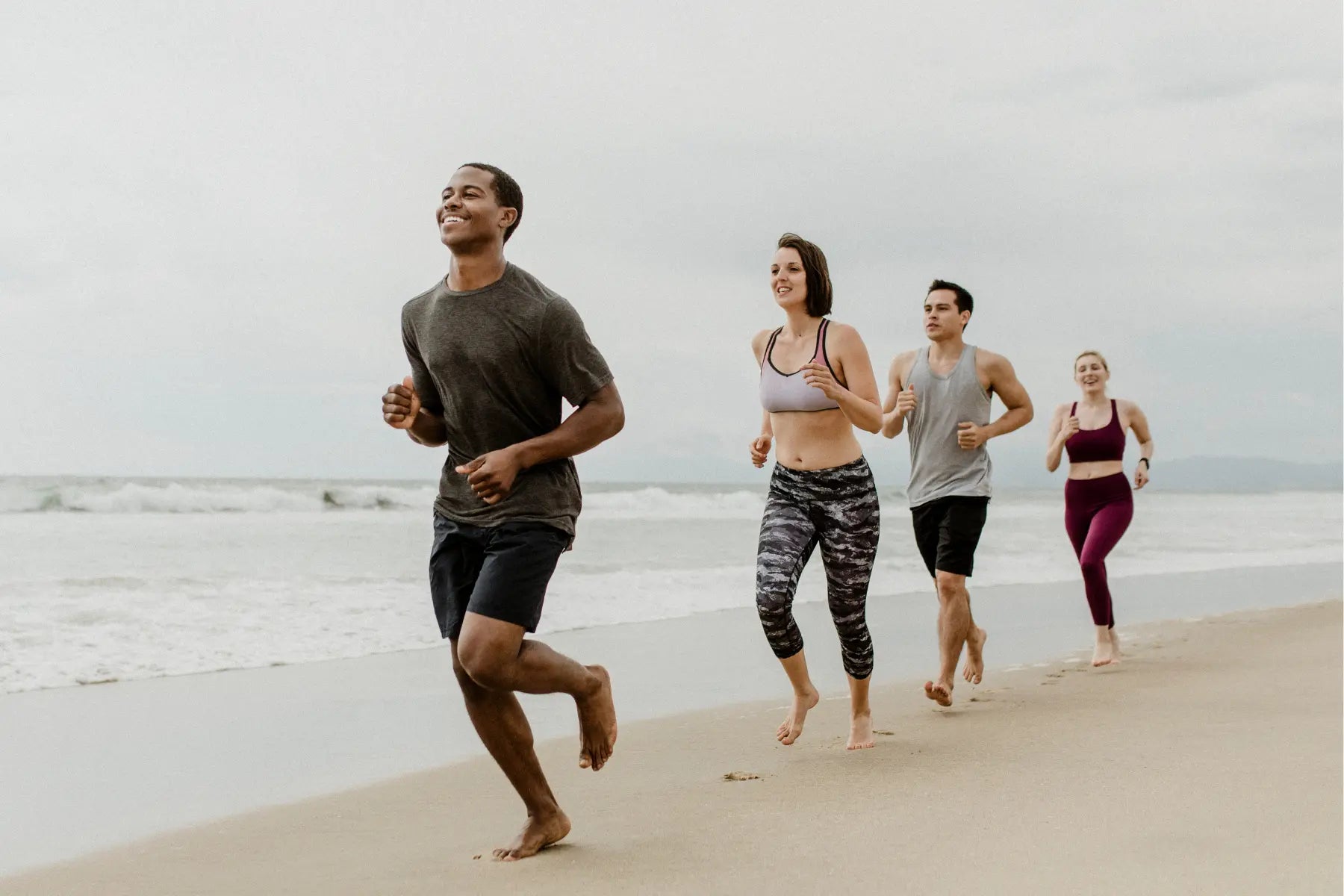 DEXA scans support fitness goals for a group of active people running barefoot along a beach shoreline.