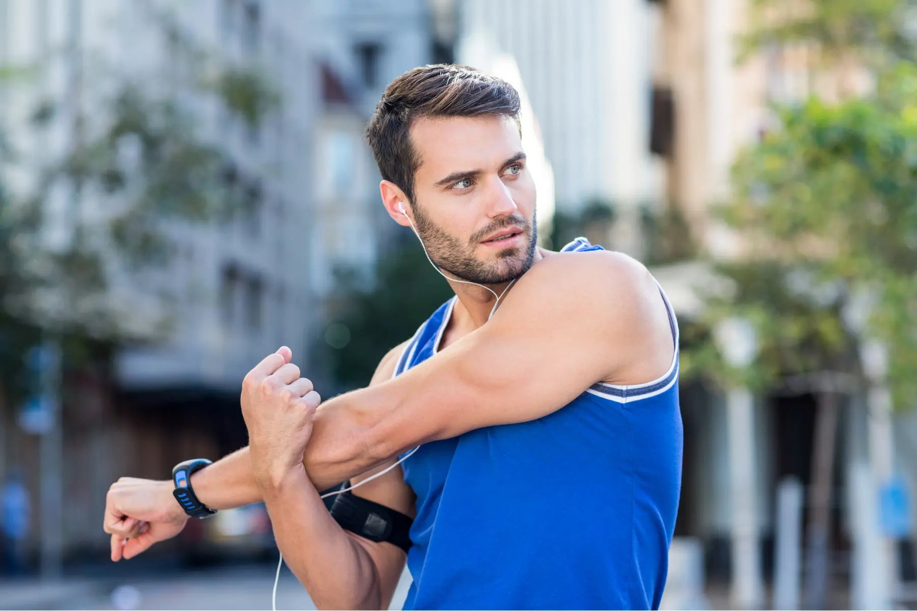 Fitness body scan preparation as man in athletic gear stretches his arm outdoors wearing fitness tracker and heart rate monitor.