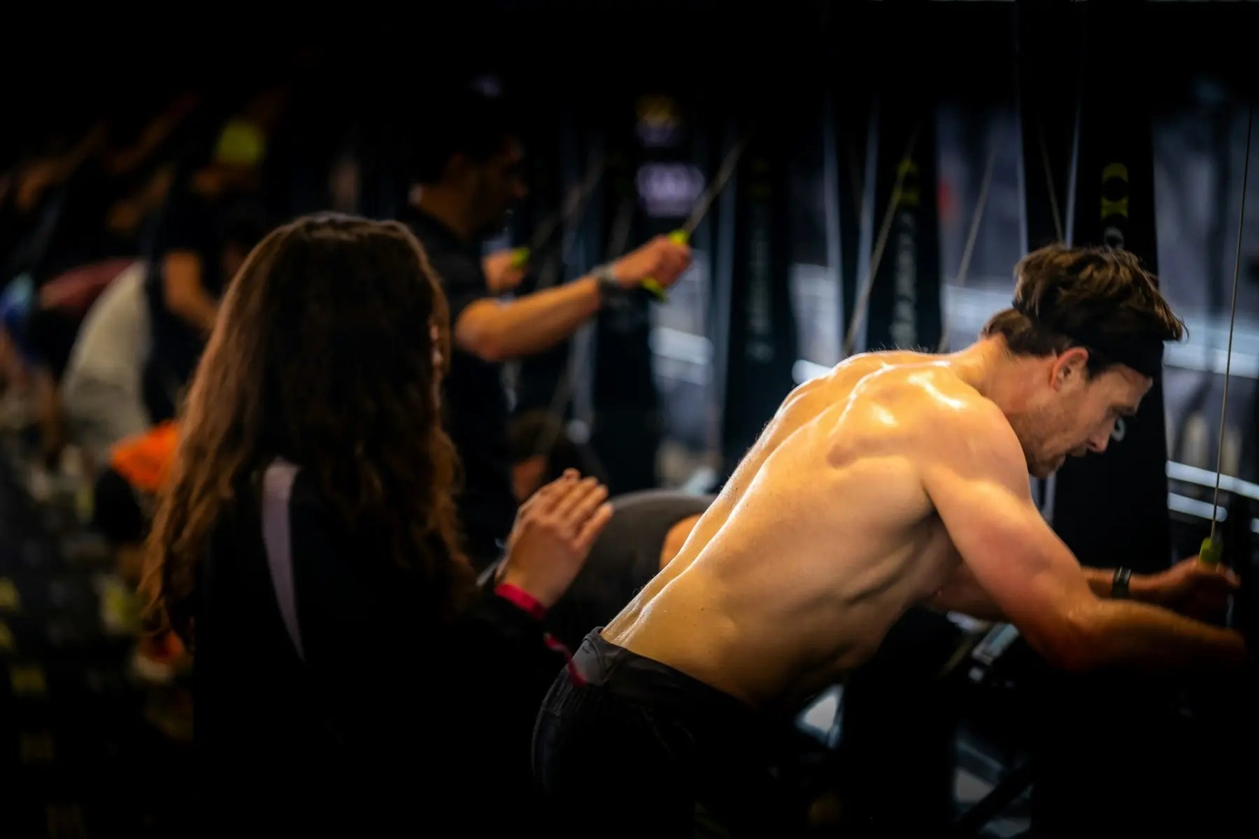 Shirtless athlete pulling a cable machine during an intense HYROX workout testing strength and endurance in a dark gym.