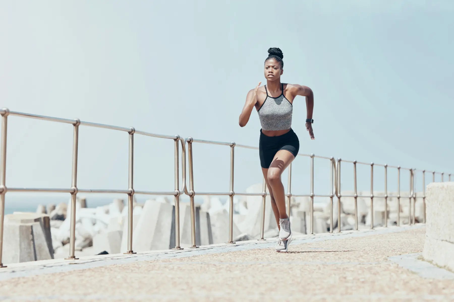VO2 max test training as athletic woman sprints along a coastal path wearing fitness gear and a smartwatch.