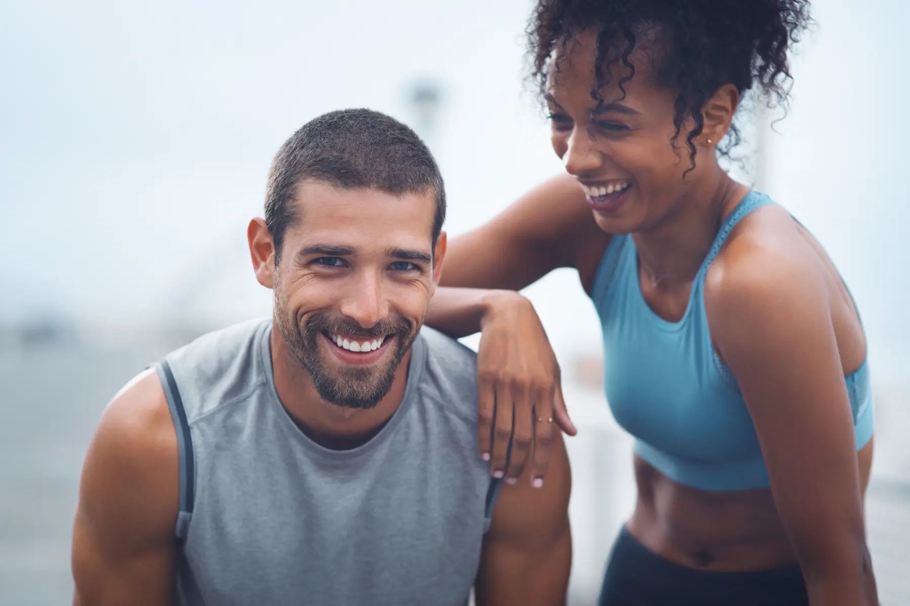 A smiling man and woman in workout clothes standing close together outdoors after exercising.