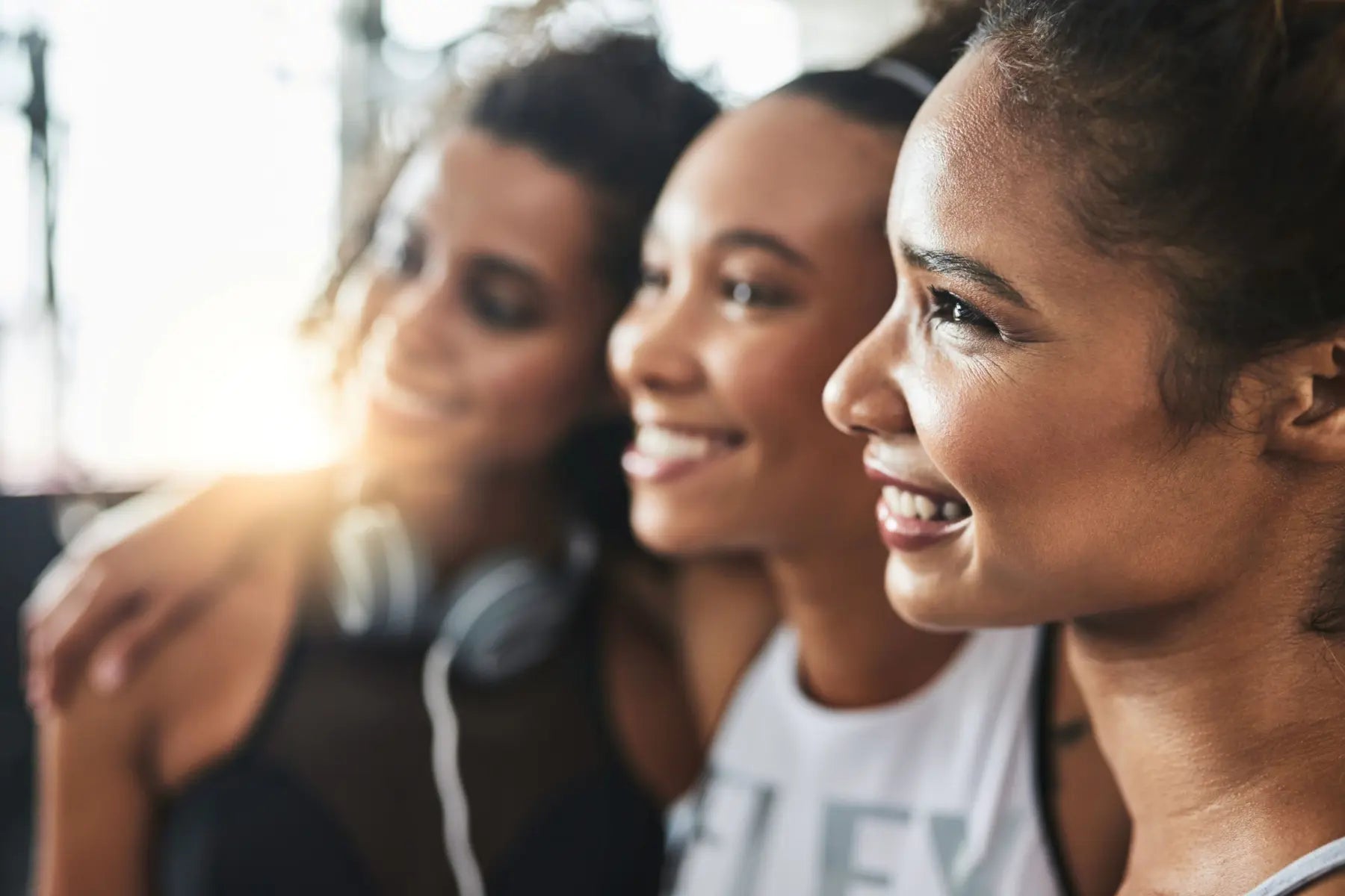 Three smiling women in activewear standing close together after a workout, supporting healthy body composition.