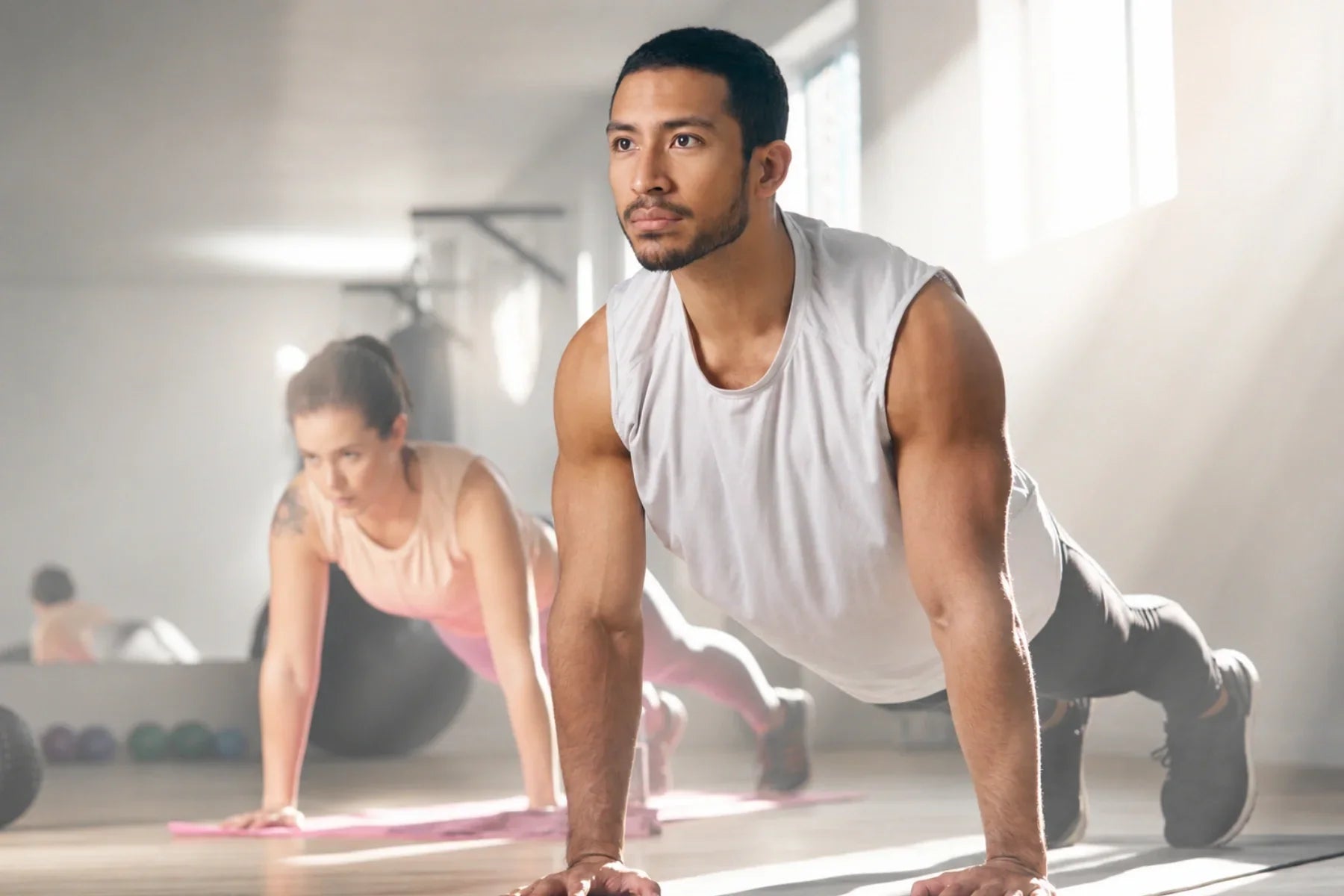 Man and woman holding push-up plank positions on mats in a bright gym during a bodyweight workout.