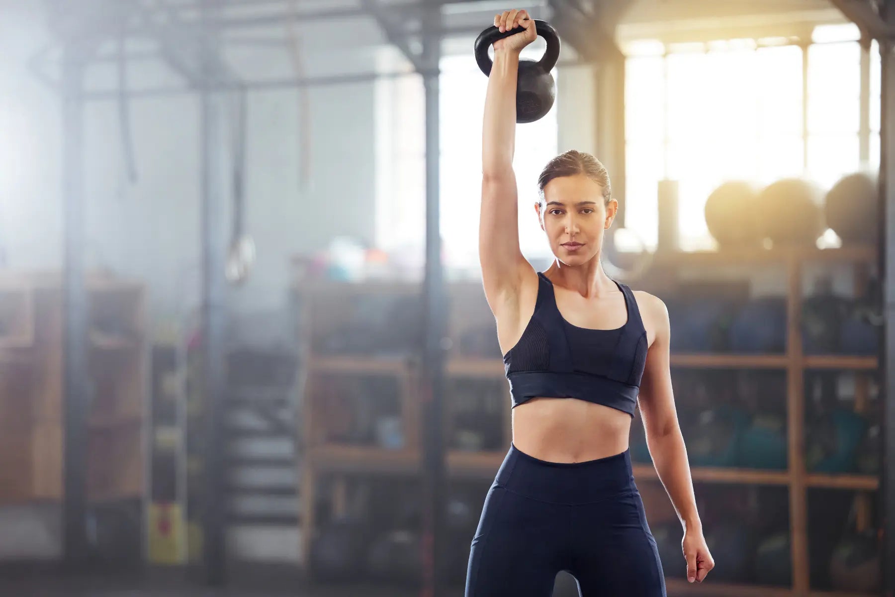 Bone density training with a woman lifting a kettlebell overhead to strengthen muscles and bones.