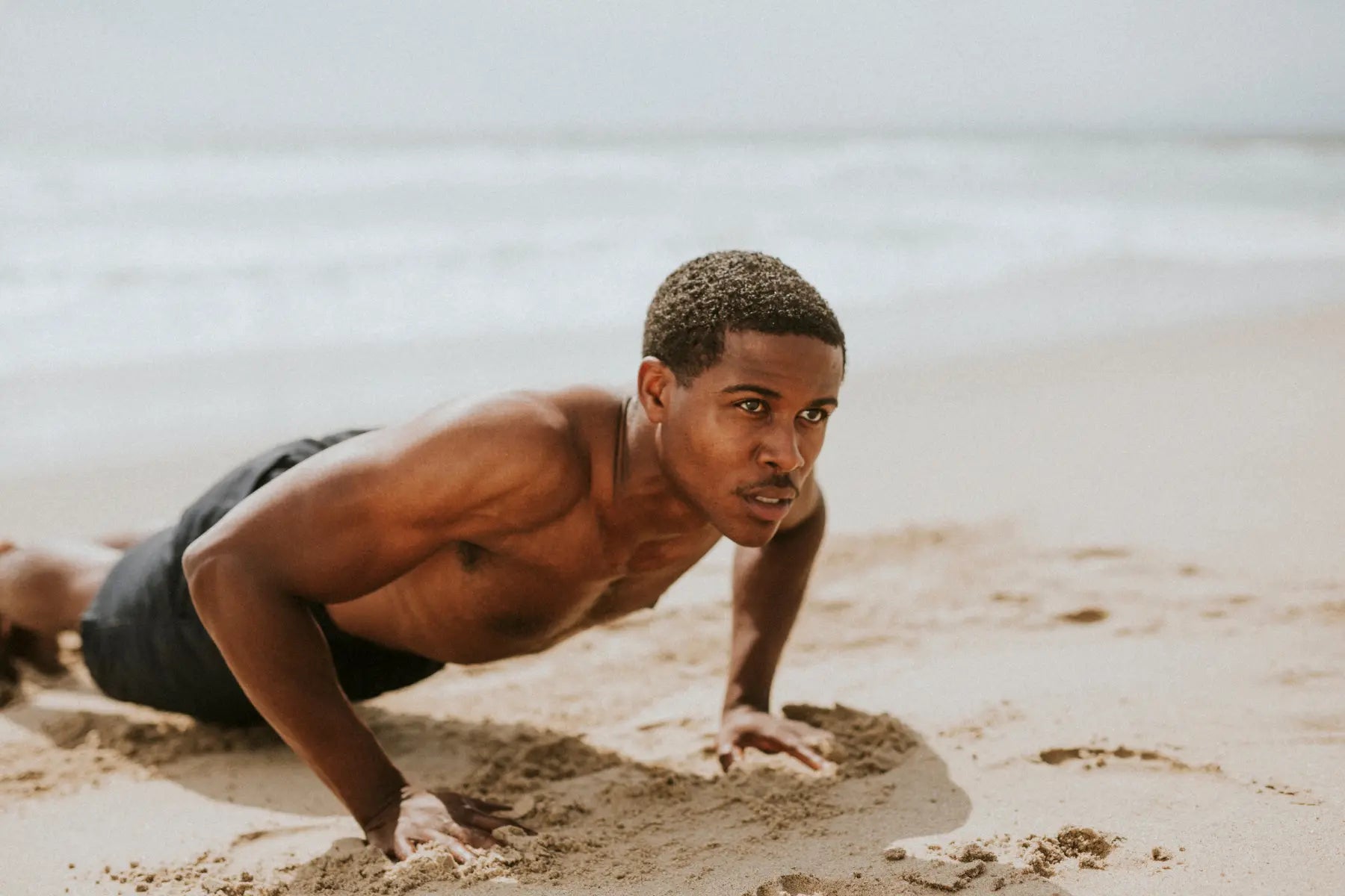 Bone density and aging exercise showing a fit man doing push-ups on the beach to strengthen muscles and bones