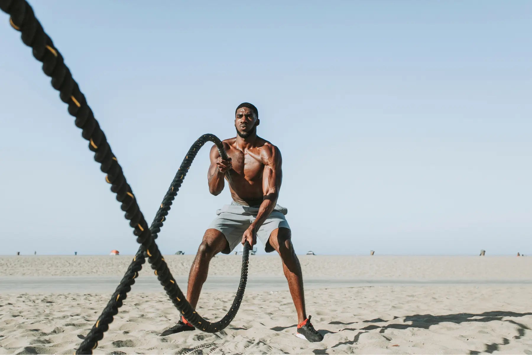 Bone density test relevance shown by man doing intense rope training on the beach for bone and muscle strength.
