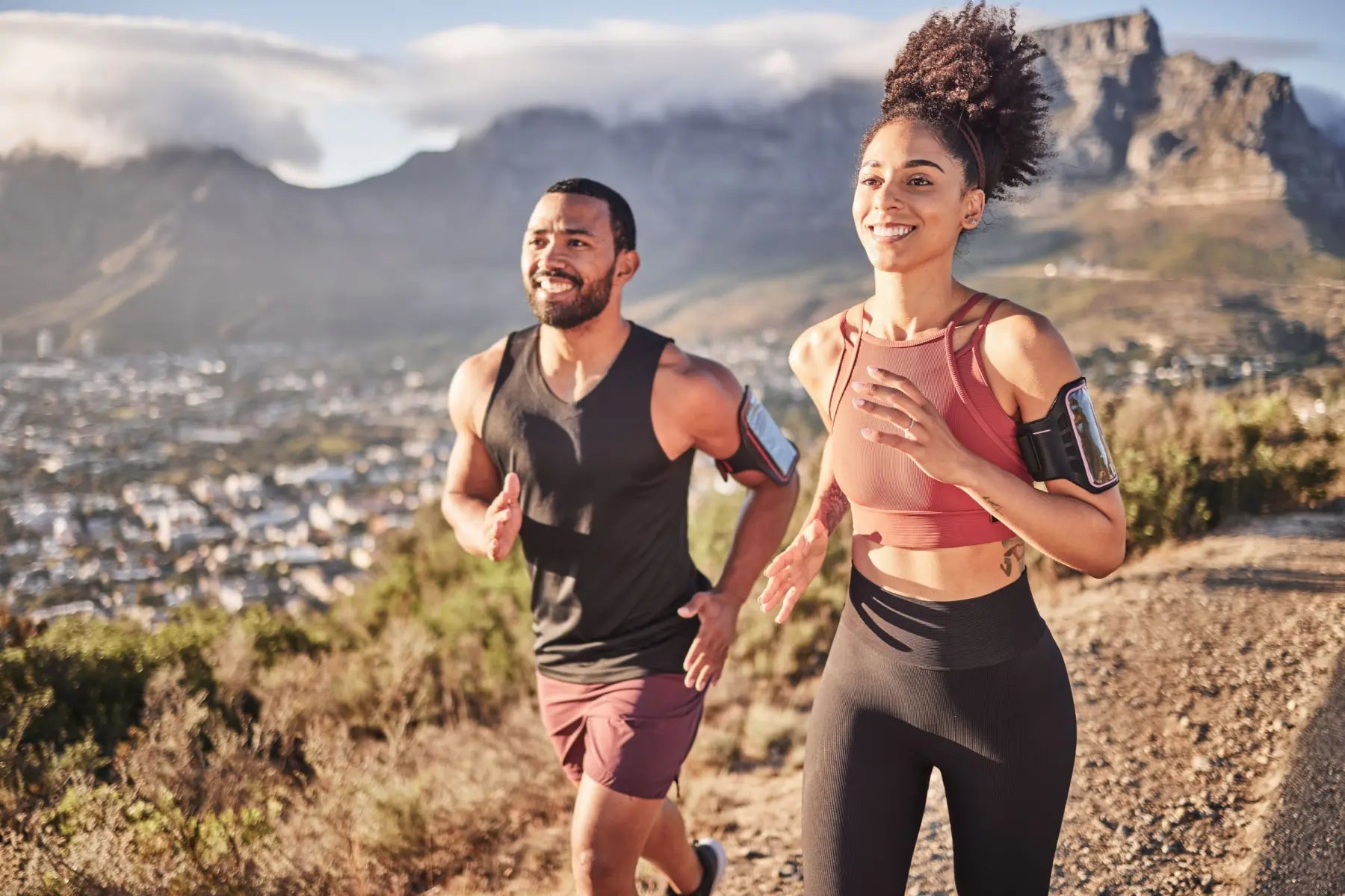 Smiling man and woman in activewear running outdoors on a mountain trail to build cardiovascular fitness.