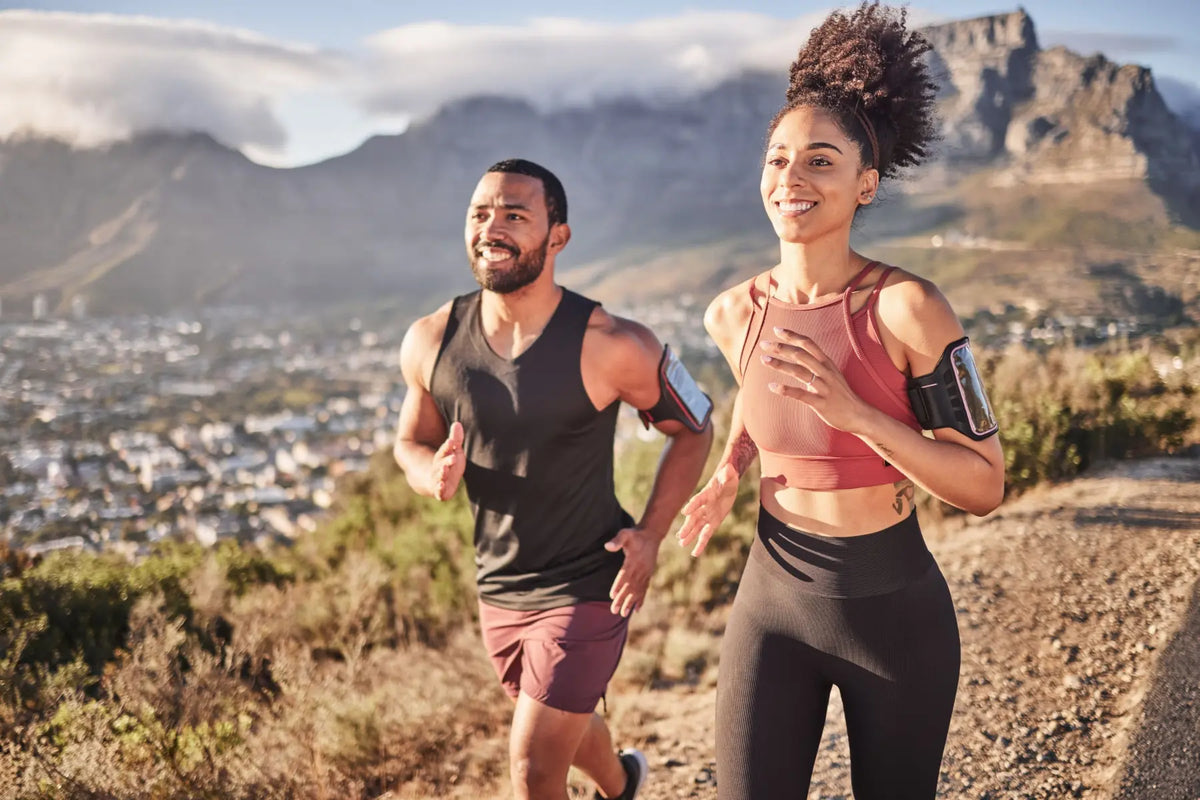 Smiling man and woman in activewear running outdoors on a mountain trail to build cardiovascular fitness.