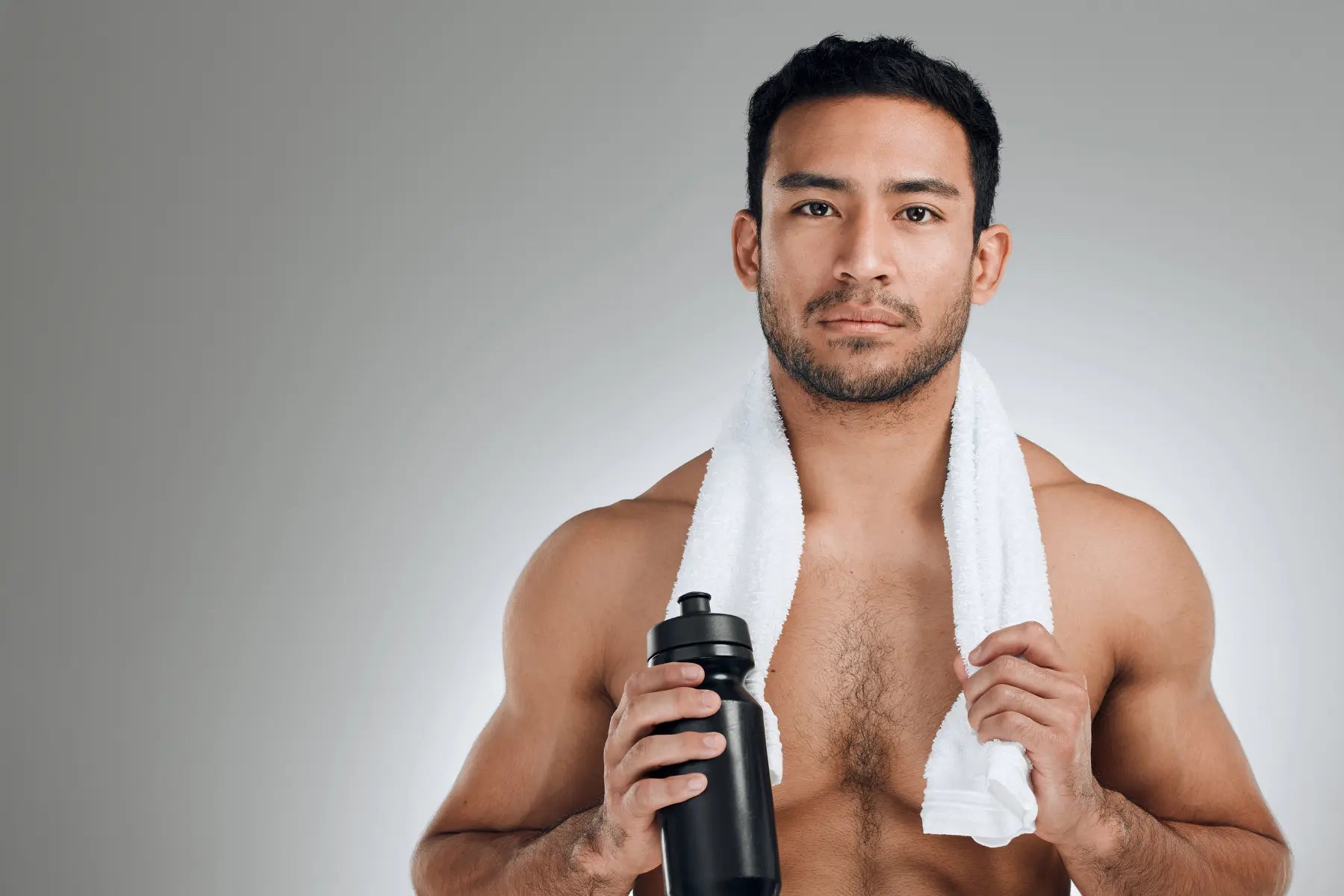 Creatine for weight loss concept image showing a fit man with a white towel around his neck holding a black water bottle against a gray studio background.