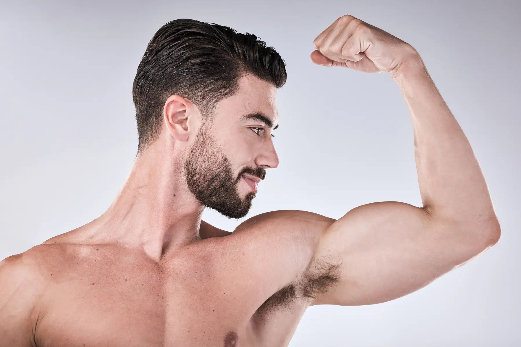 GLP-1 muscle loss risk illustrated by a lean bearded man flexing his bicep against a gray studio background.