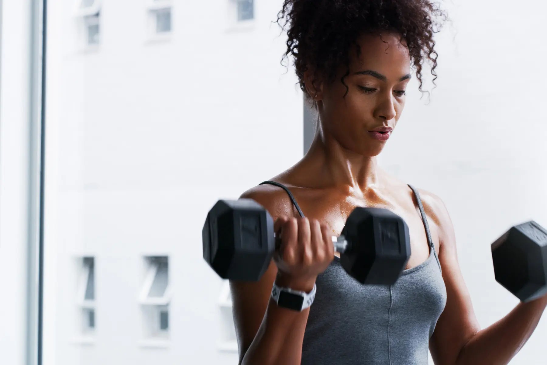 GLP-1 weight loss supported by strength training as a woman performs dumbbell bicep curls in a bright gym.