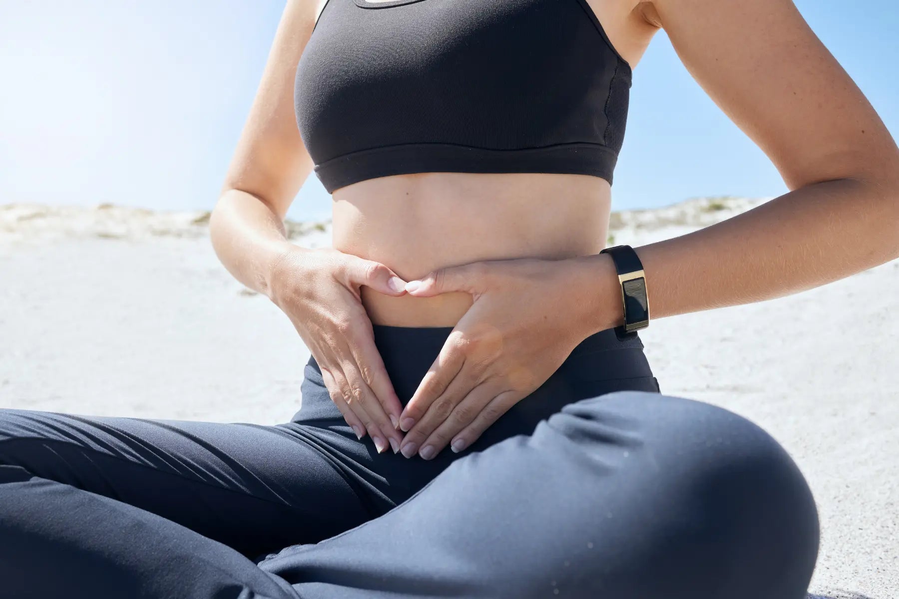 Gut health and immunity symbolized by a woman forming a heart shape over her stomach while sitting outdoors.