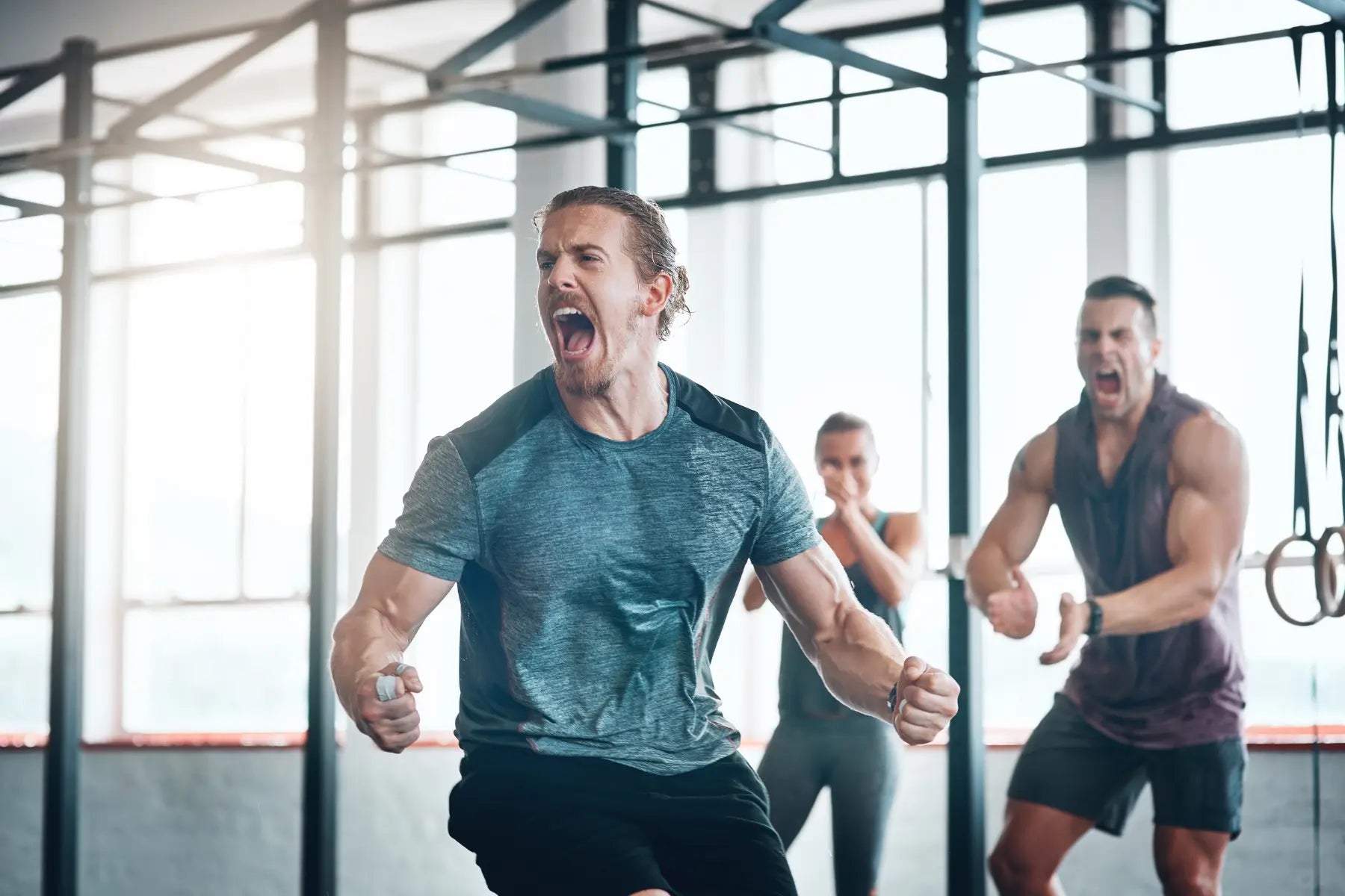 VO2 max training intensity on display as three athletes shout and pump their fists during a high-intensity gym session.