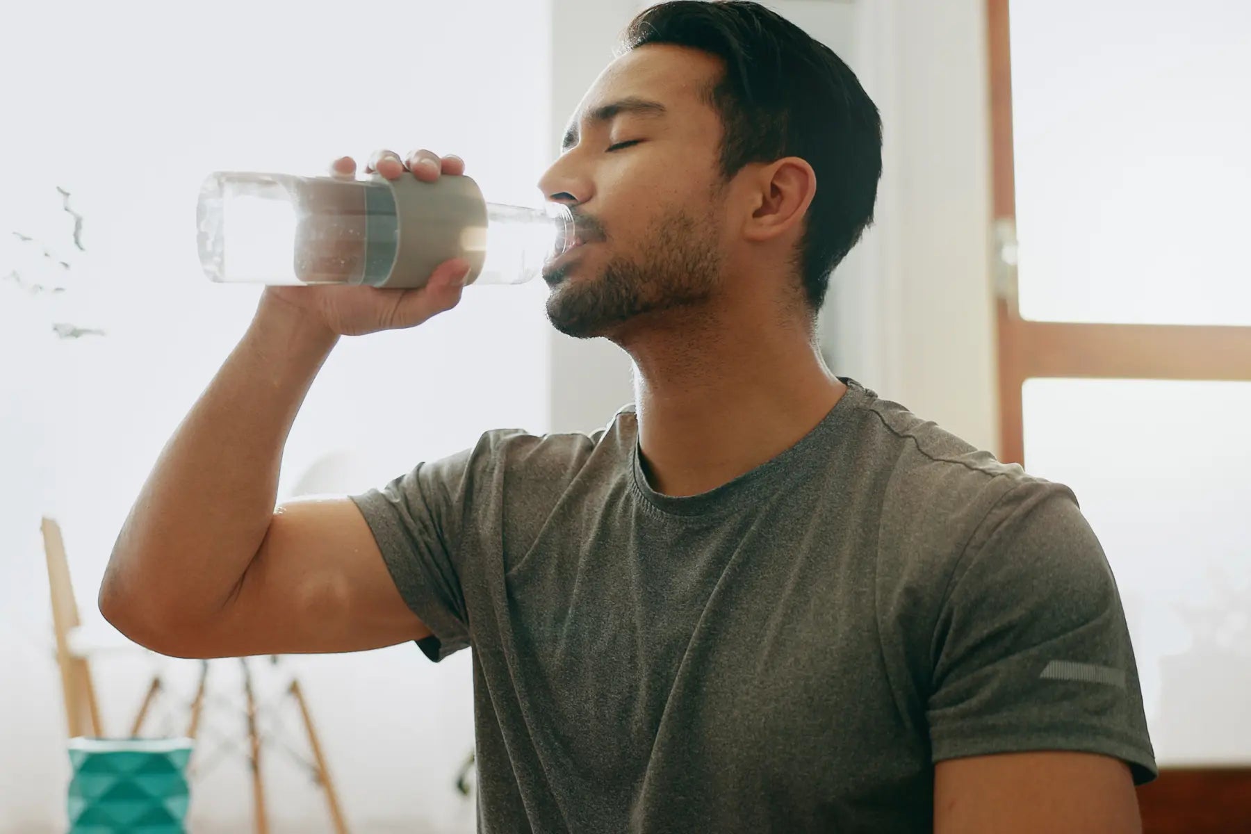 DEXA body composition insights support hydration and fitness, shown by man drinking water after a workout indoors.
