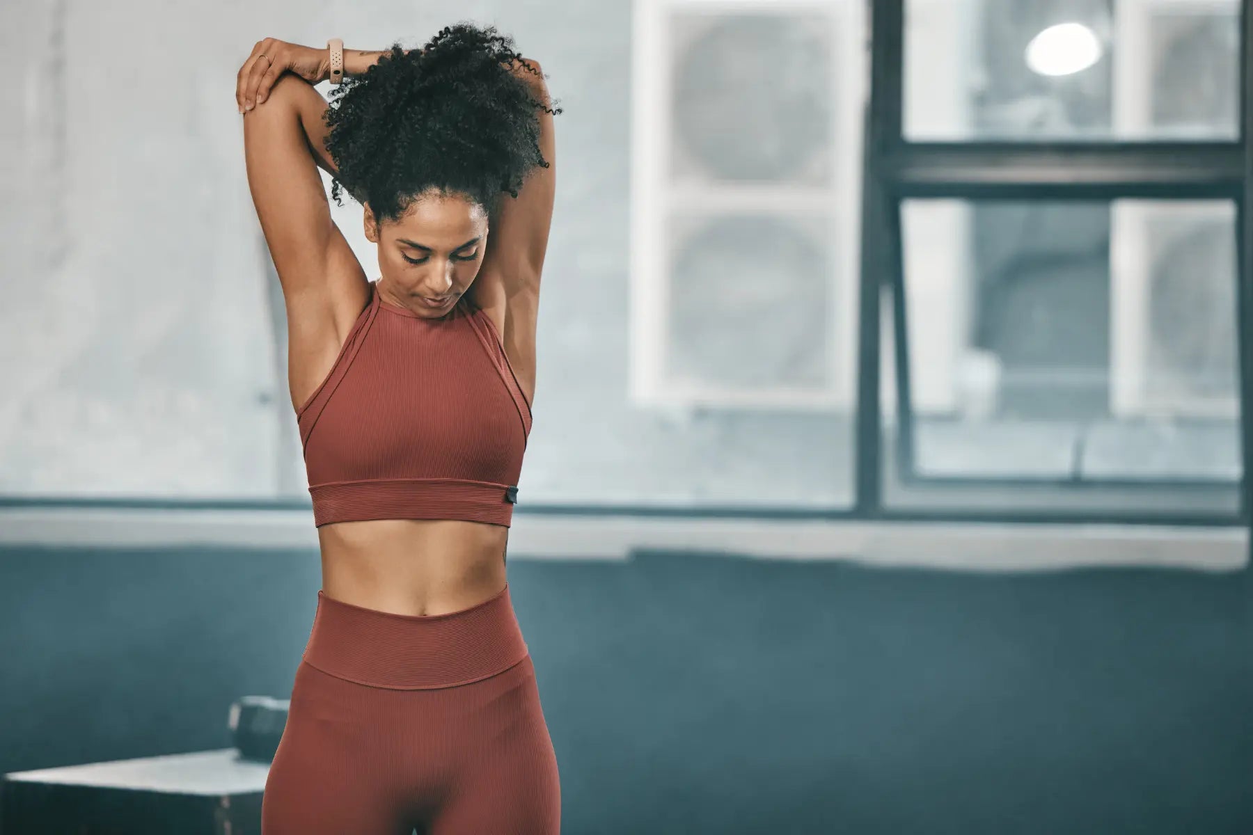 Lean body mass highlighted by fit woman stretching arms in athletic wear at indoor gym.