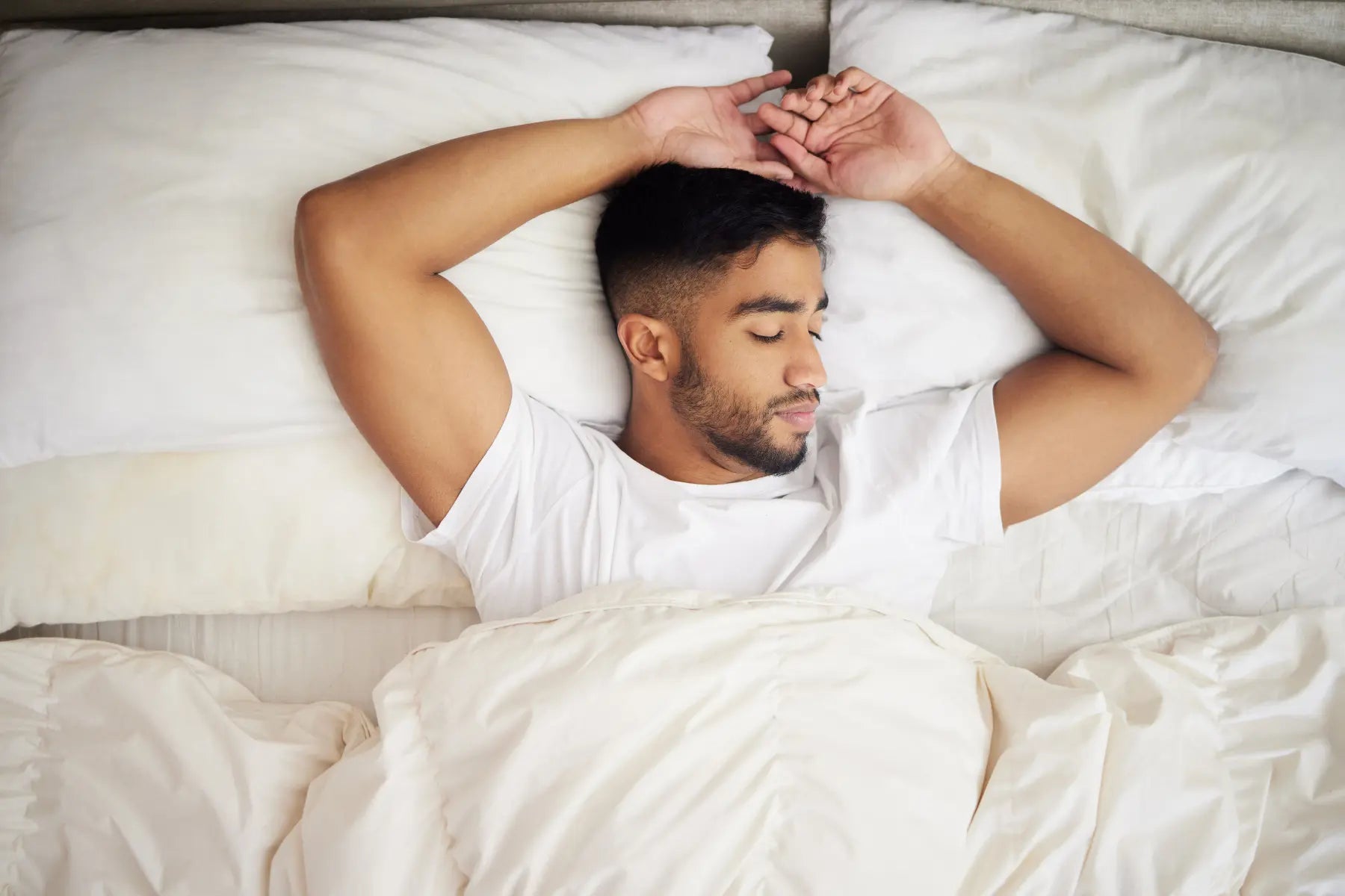 Man in a white t-shirt sleeping peacefully in a bed with white bedding, resting better with magnesium for sleep.