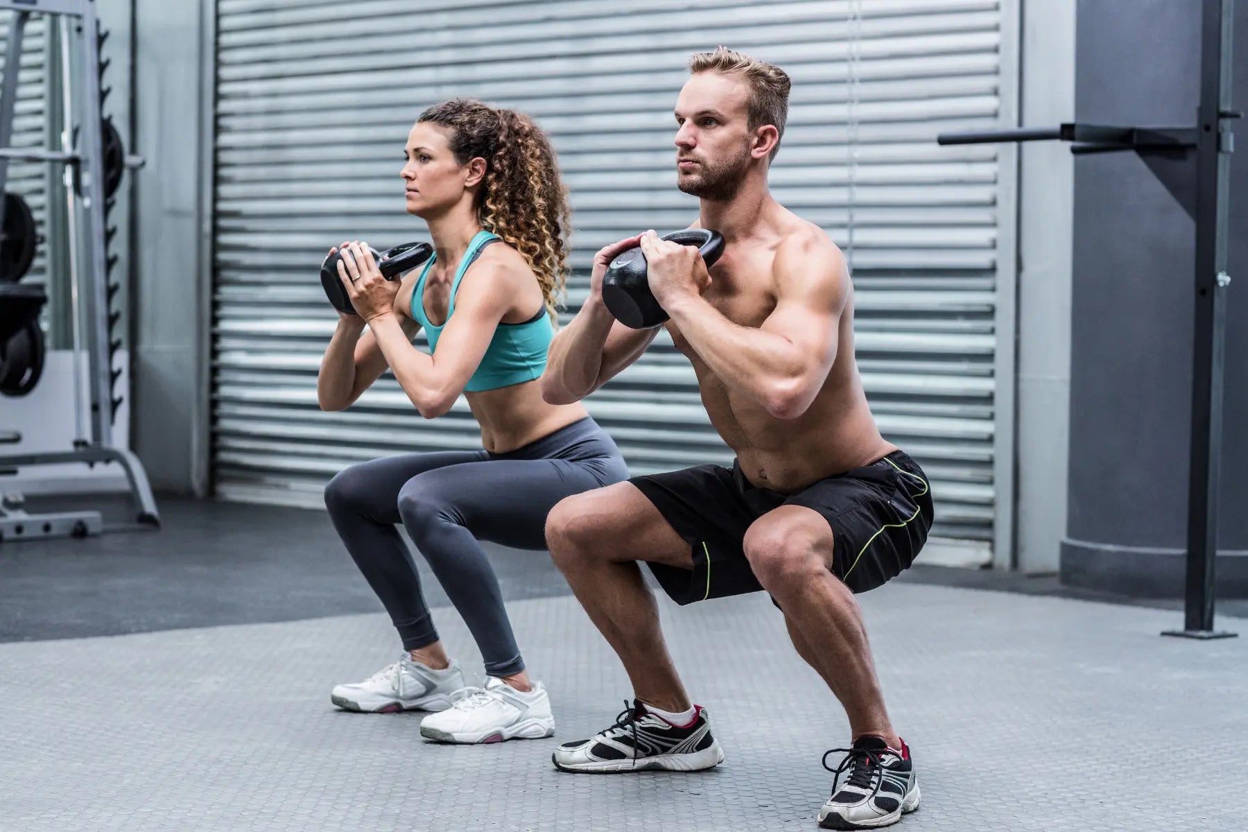Man and woman performing goblet squats with kettlebells in a gym