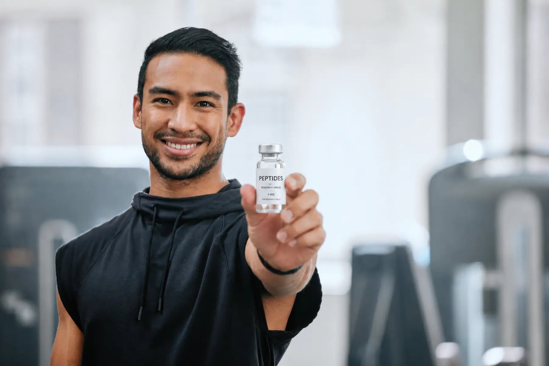 Research-grade peptides held up in a 5 mg vial by a smiling man in a gym.