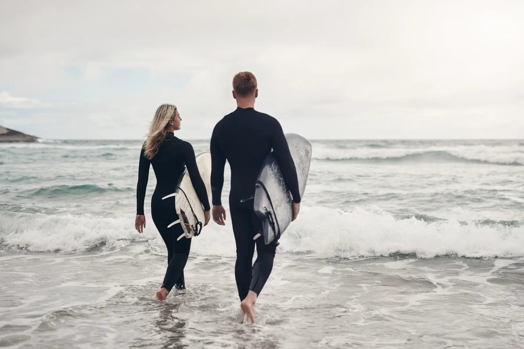 Sustainable weight loss starts with active habits like surfing, shown by two people walking into ocean with surfboards.