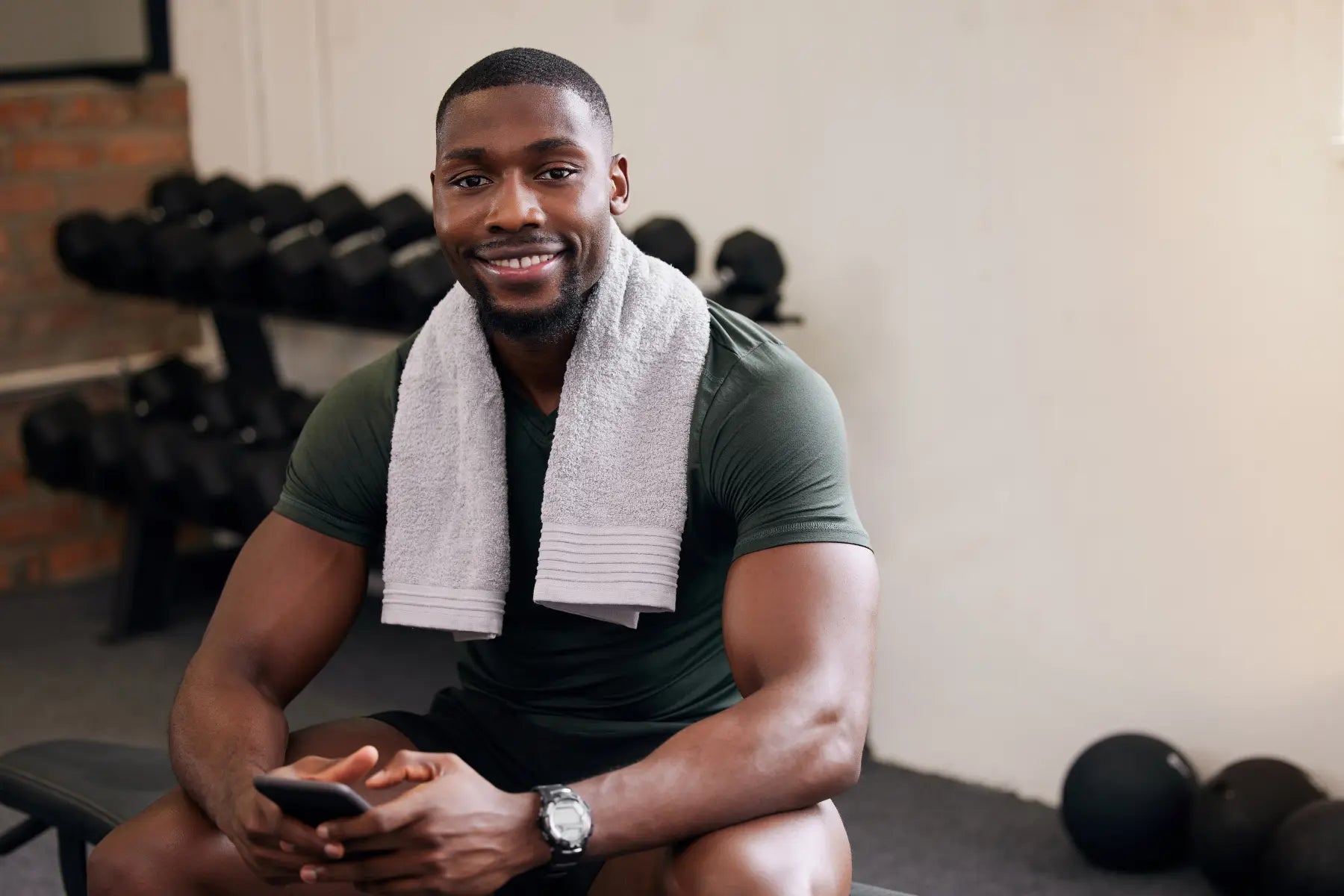 Testosterone decline in men depicted by a fit man resting on a gym bench with a towel around his neck and dumbbells in the background.