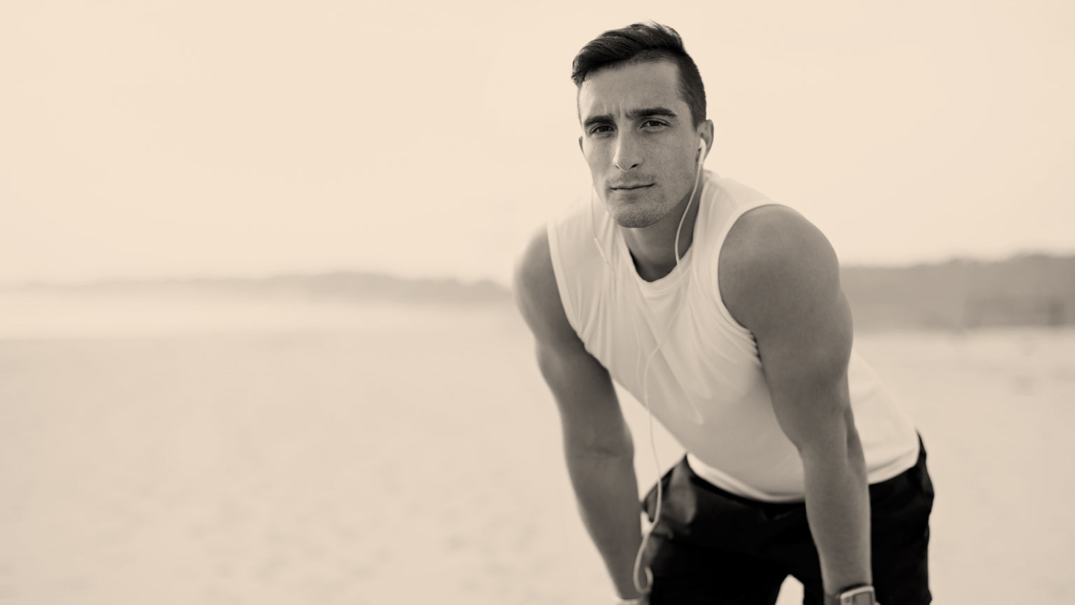 Man in a white tank top and black shorts standing on a beach.