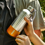 Person holding a silver and orange thermos outdoors