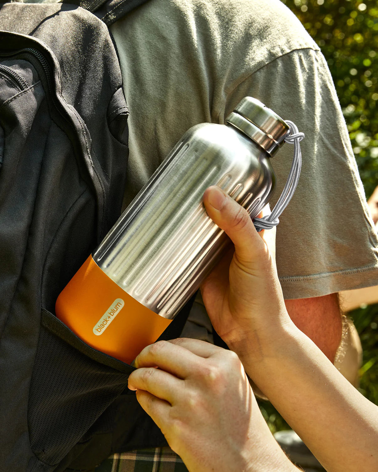 Person holding a silver and orange thermos outdoors
