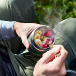 Person holding a jar of food with raspberries and other ingredients outdoors