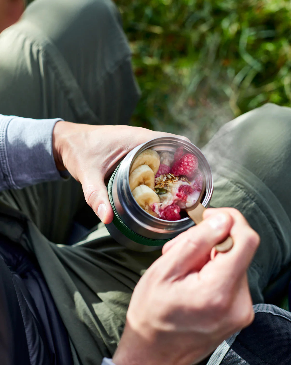 Person holding a jar of food with raspberries and other ingredients outdoors