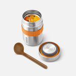 Stainless steel food container with orange grip, wooden spoon, and small white container on a light gray background